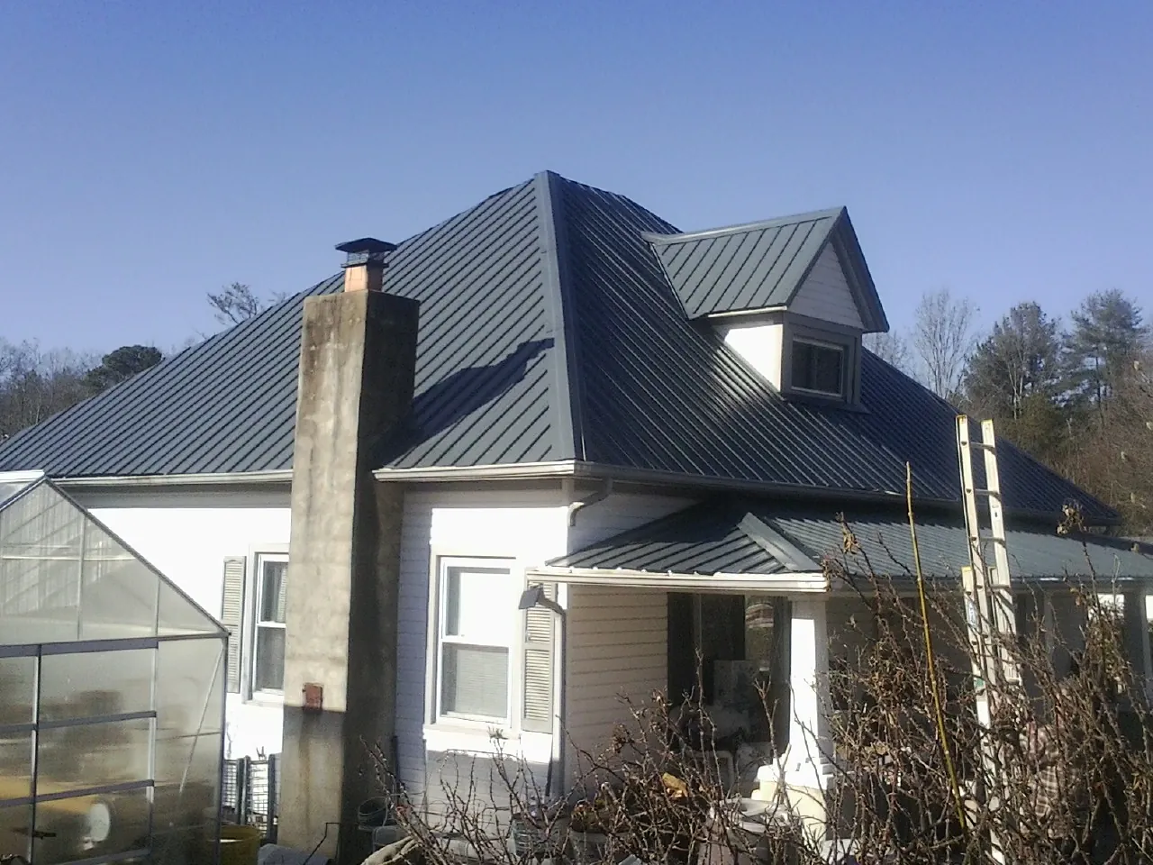 Dark blue standing seam metal roof on a white farmhouse with dormer in Anadarko