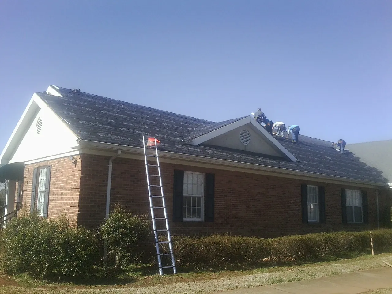 Crew tearing shingles off a brick ranch roof with a ladder set — Emergency Roof Repair work by our crew in Anadarko