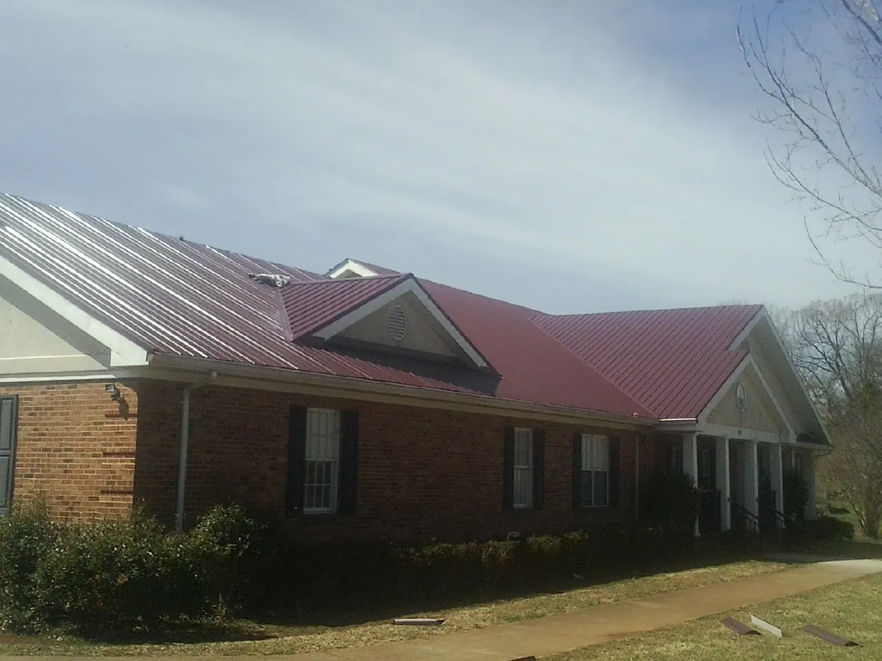 Red metal roof with gabled entries on a long brick building, from a Hail Damage Roof Repair job in Anadarko