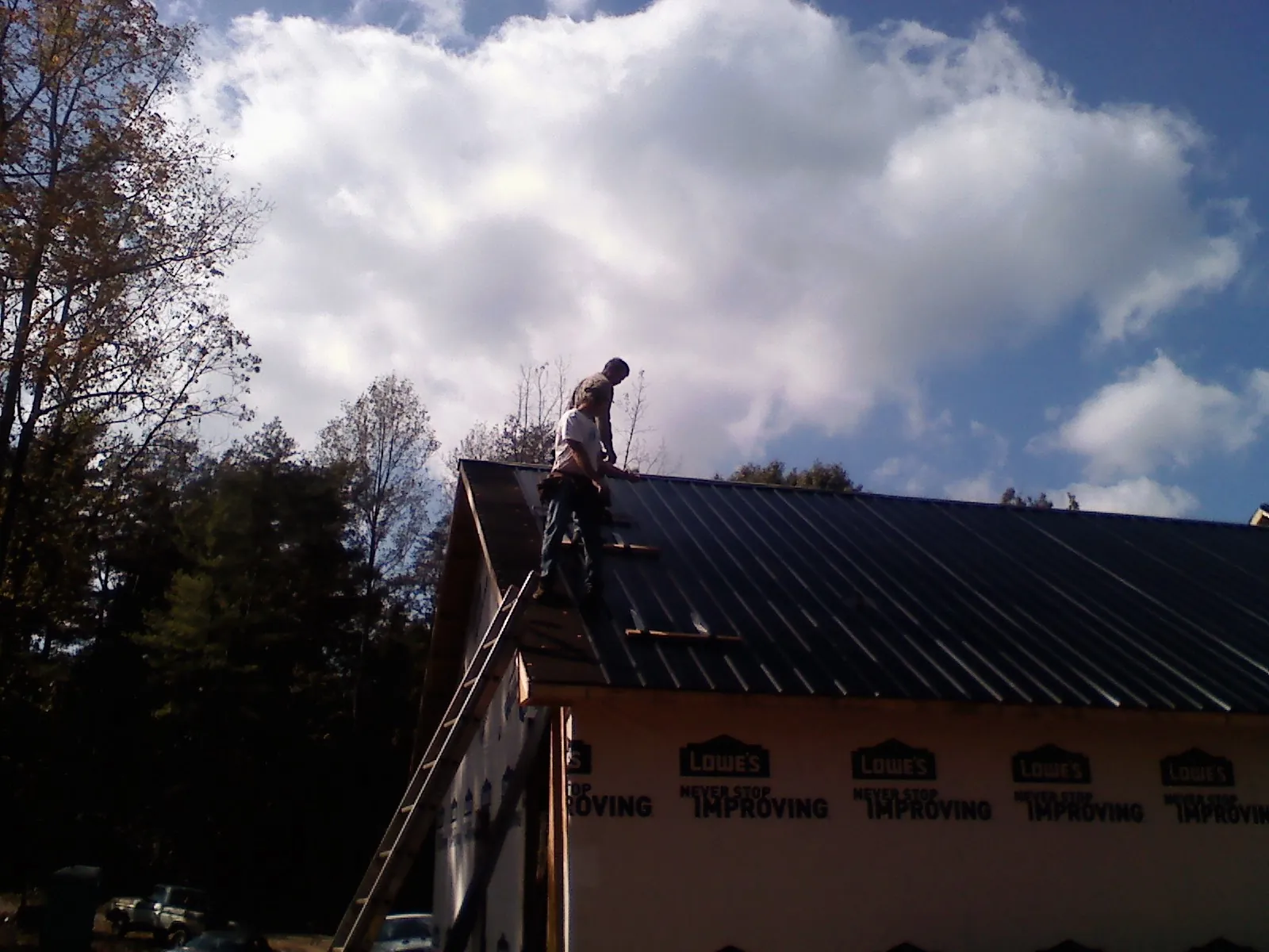 Roofer fastening dark metal panels high against a cloudy sky, from a Roof Inspection job in Anadarko
