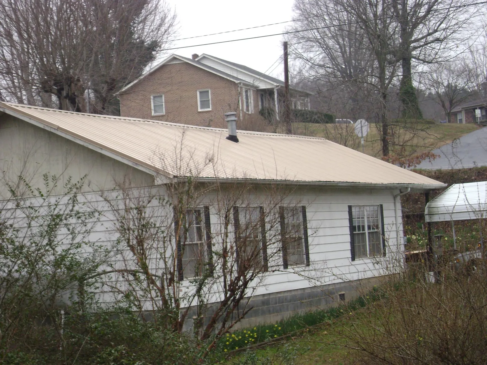 Tan metal roof on a white sided house set into a hillside — Commercial Roofing by Roofing Brothers in Anadarko